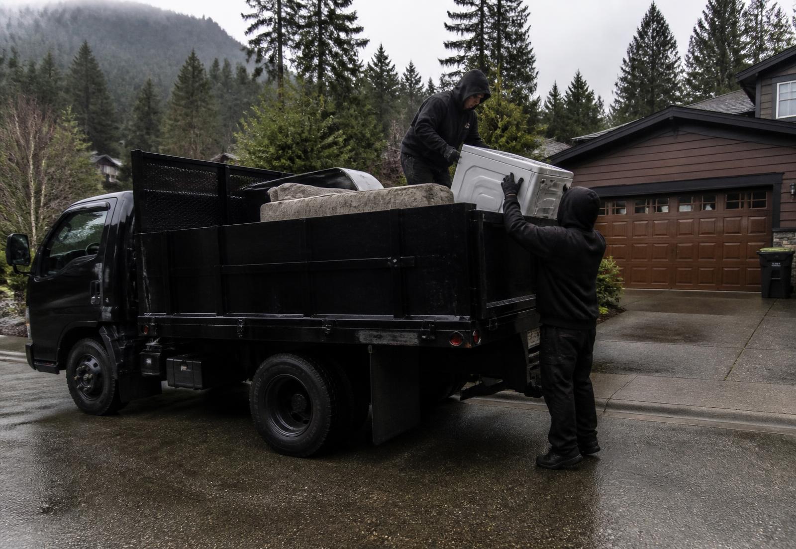253 Junk crew loading an old sofa and washing machine into a black junk removal truck in a Tacoma, Washington driveway